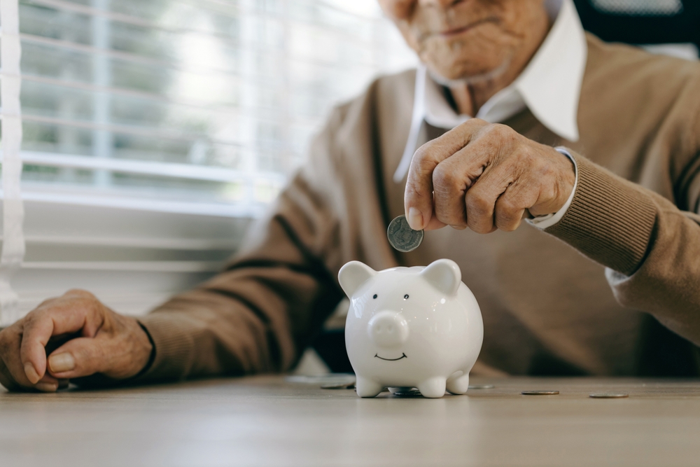 Saving money investment for future. old man hand putting money coins in a piggy bank